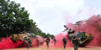 Soldiers running from armored vehicles with red smoke