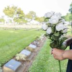 Person holding white roses at a cemetery