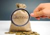 Hand holding magnifying glass over sack labeled Sanctions