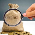 Hand holding magnifying glass over sack labeled Sanctions