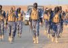 Camouflaged soldiers wearing masks and vests walk in desert