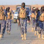 Camouflaged soldiers wearing masks and vests walk in desert