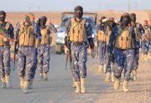 Camouflaged soldiers wearing masks and vests walk in desert