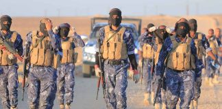 Camouflaged soldiers wearing masks and vests walk in desert