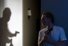 Man with gun watches shadow of armed figure