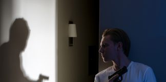Man with gun watches shadow of armed figure