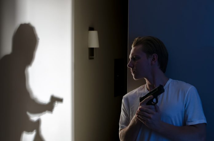 Man with gun watches shadow of armed figure