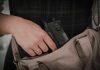 Hand placing handgun into beige handbag