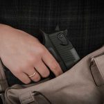 Hand placing handgun into beige handbag