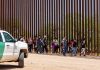 People walking beside tall fence and border patrol vehicle