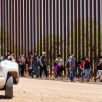 People walking beside tall fence and border patrol vehicle