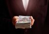 Hand holding a stack of hundred-dollar bills