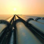 Industrial pipes extending towards the horizon over water during sunset