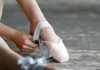 Ballet dancer tying pointe shoes in a studio