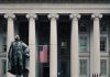 US Treasury Department building with statue and flag.