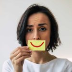 Woman holding smiley face card over mouth