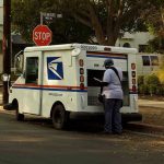USPS mail carrier at truck near stop sign