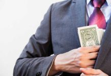 Person in suit putting dollars in jacket pocket