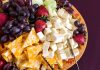 A colorful cheese and fruit platter featuring various cheeses and fresh fruits