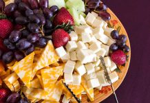 A colorful cheese and fruit platter featuring various cheeses and fresh fruits