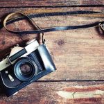 A vintage camera resting on a wooden surface with a leather strap