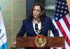 Person speaking at podium with flags in background.