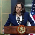 Person speaking at podium with flags in background.
