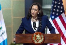 Person speaking at podium with flags in background.