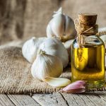 A bottle of olive oil surrounded by garlic cloves on a burlap background