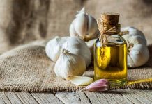 A bottle of olive oil surrounded by garlic cloves on a burlap background