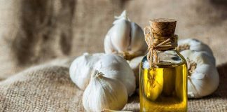 A bottle of olive oil surrounded by garlic cloves on a burlap background