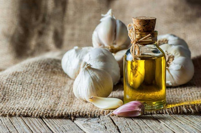 A bottle of olive oil surrounded by garlic cloves on a burlap background