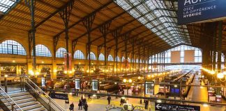 Interior view of a busy train station with large windows and a staircase