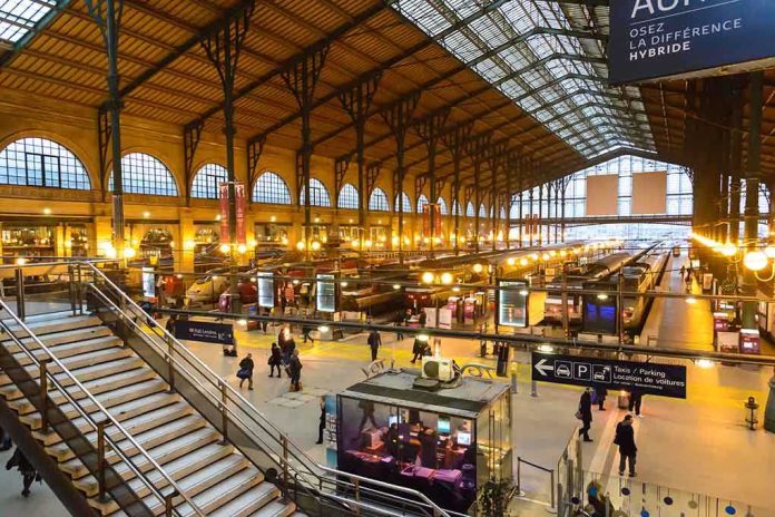 Interior view of a busy train station with large windows and a staircase