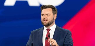 Man speaking at a podium, wearing suit and tie.
