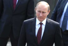 Putin Reveals Parades Nuke – Global Panic! A serious-looking man in a suit walking outdoors with security personnel in the background