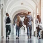 AI Cheating Wave ROCKS Top University! Four students walking in a corridor together.