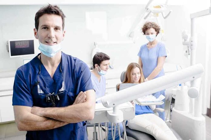 A dentist smiling in a dental office with a team assisting a patient