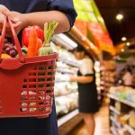 Person holding a basket filled with colorful vegetables in a supermarket