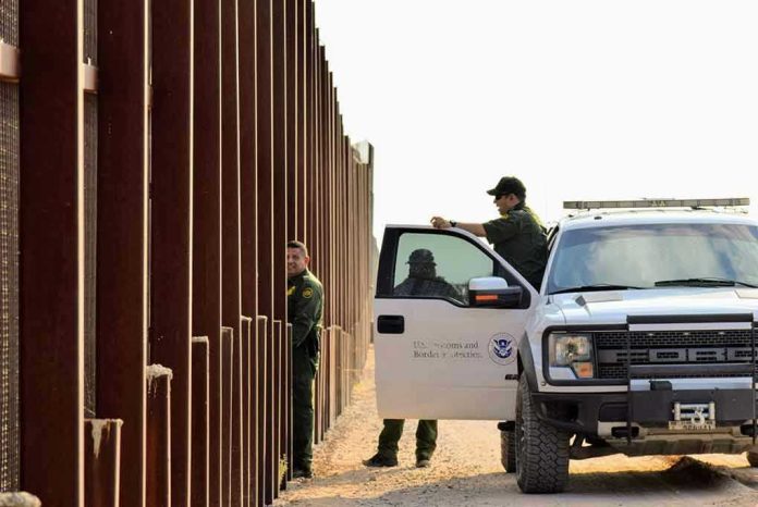 1545833798 Border patrol agents near a tall metal fence.