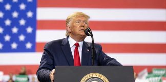 Man speaks at podium with U.S. flag background.