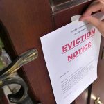 Hand tacking eviction notice on a wooden door.