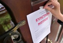 Hand tacking eviction notice on a wooden door.