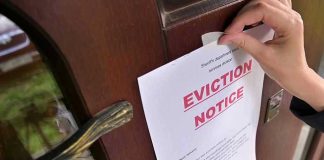 Hand tacking eviction notice on a wooden door.