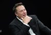 Musk UNLEASHES Legal War Over Restroom Rights Man in suit smiling, resting chin on hand.