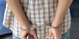 A person in handcuffs viewed from behind, wearing a plaid shirt and denim jeans