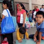 American Child DEPORTED – Constitutional Crisis EXPLODES People waiting outside carrying bags, boys sitting and playing.
