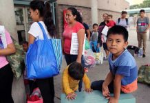 People waiting outside carrying bags, boys sitting and playing.
