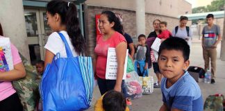 People waiting outside carrying bags, boys sitting and playing.