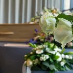 Fashion ICON Dies- Entire Industry Crumbles White roses in front of a casket.